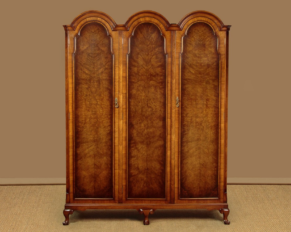 A 1920s Queen Anne style triple-door combination wardrobe made of figured burr walnut veneer with triple arched cornices and cabriole legs.