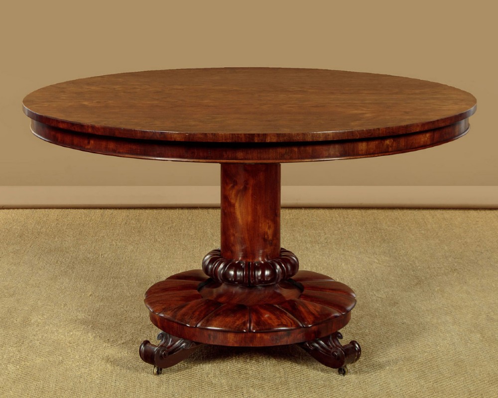 An early Victorian circular mahogany breakfast table with a central pedestal and lobed base supported by scroll feet on brass castors.