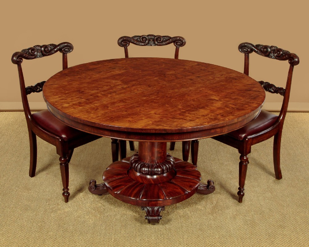 An early Victorian circular mahogany breakfast table with a central pedestal and lobed base supported by scroll feet on brass castors. View II