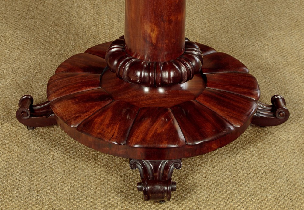An early Victorian circular mahogany breakfast table with a central pedestal and lobed base supported by scroll feet on brass castors. View VII