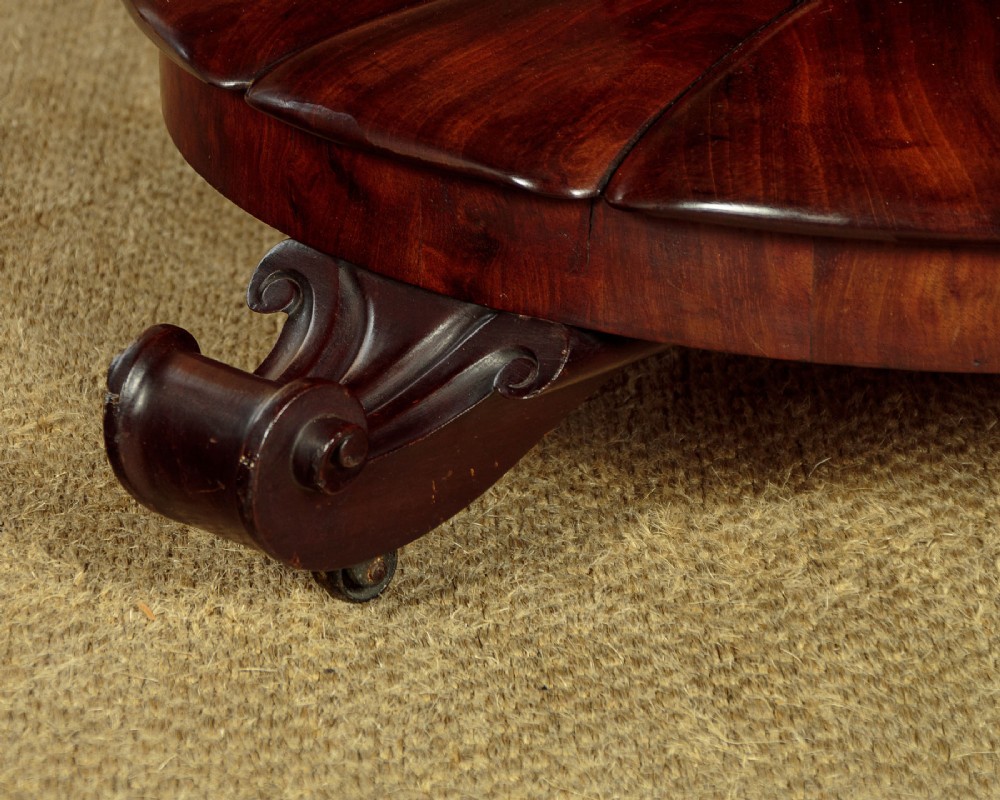 An early Victorian circular mahogany breakfast table with a central pedestal and lobed base supported by scroll feet on brass castors. View IX