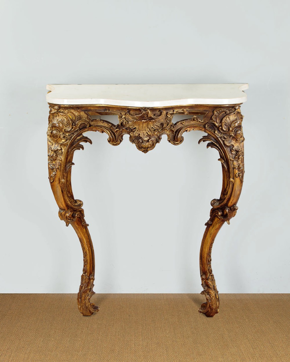 A late 19th-century Rococo Revival giltwood console table featuring carved scrollwork, two cabriole legs, and a shaped white marble top.