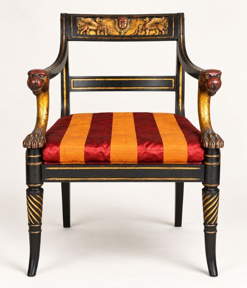 fig 1. A pair of black-painted and parcel-gilt Regency style armchairs featuring lion head arm terminals, spiral-turned front legs, and red and gold striped upholstery.
