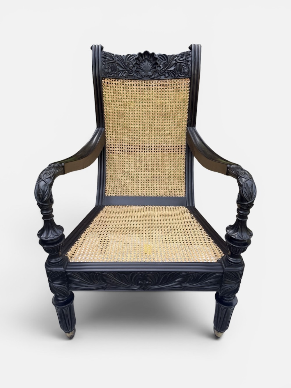 A mid-19th century carved ebony armchair featuring an intricately carved floral crest, woven natural cane seat and back, and turned fluted legs on brass castors. View III