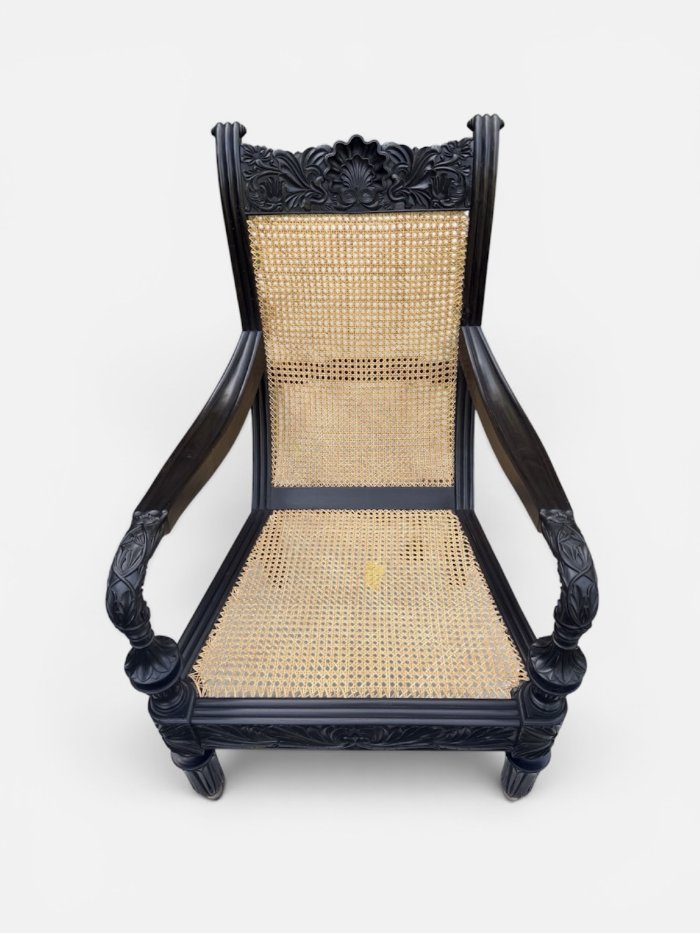 A mid-19th century carved ebony armchair featuring an intricately carved floral crest, woven natural cane seat and back, and turned fluted legs on brass castors. View IV