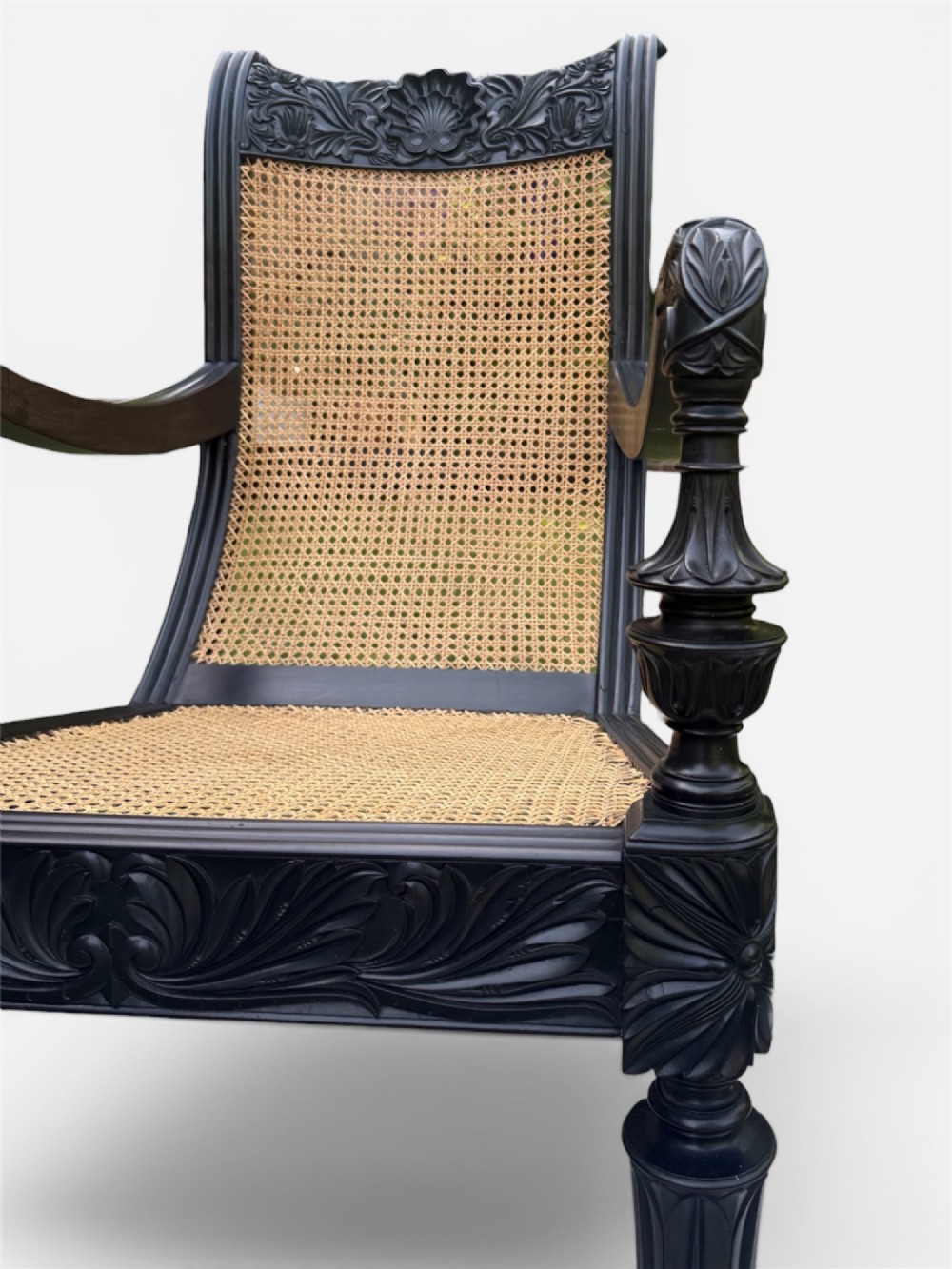 A mid-19th century carved ebony armchair featuring an intricately carved floral crest, woven natural cane seat and back, and turned fluted legs on brass castors. View V