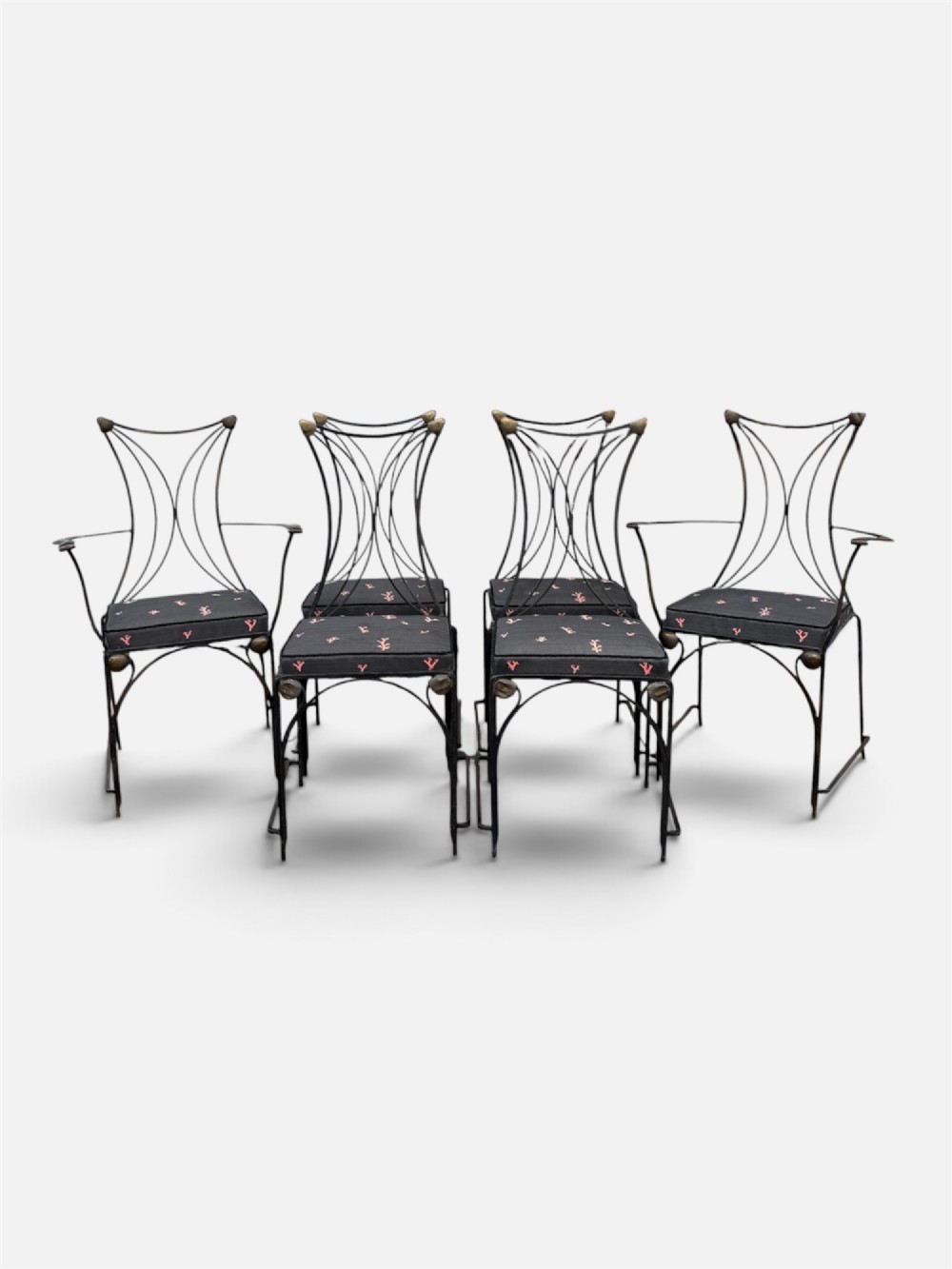 A set of six black wrought iron dining chairs featuring curved hourglass backrests, brass accents, and dark upholstered cushion seats.