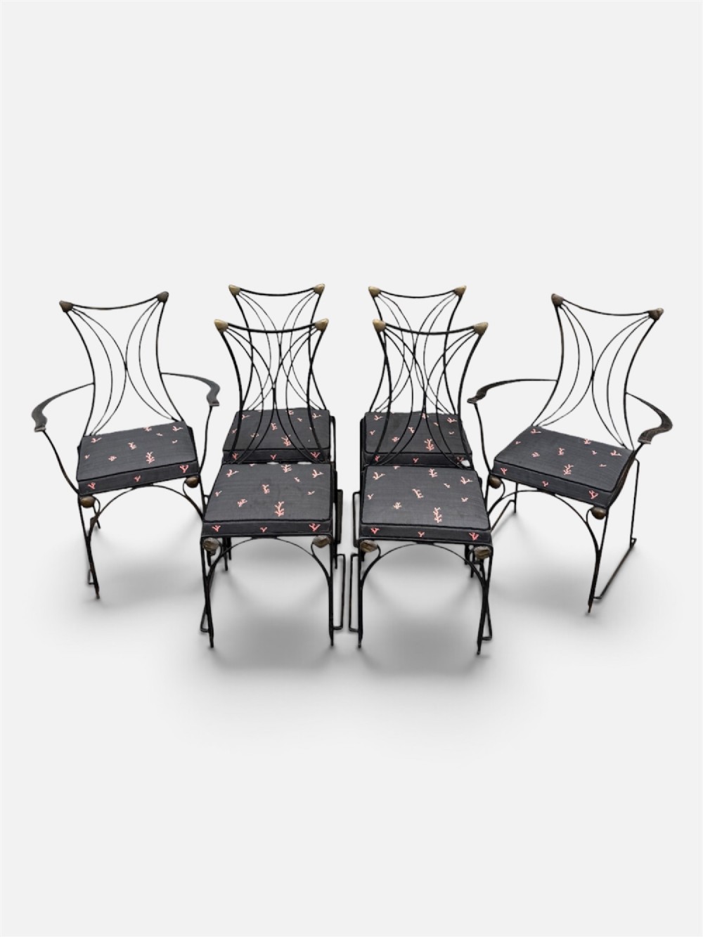 A set of six black wrought iron dining chairs featuring curved hourglass backrests, brass accents, and dark upholstered cushion seats. View II