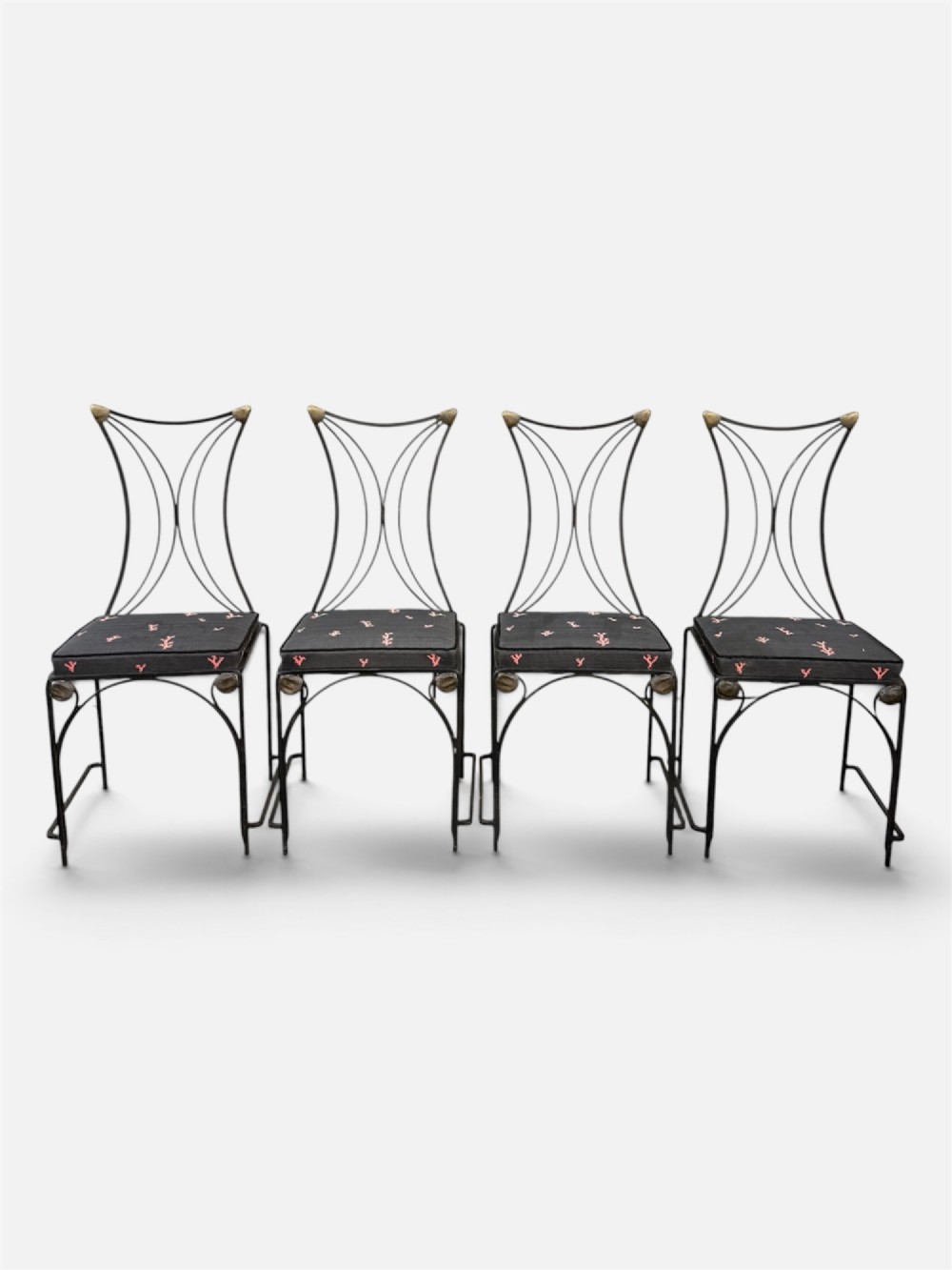 A set of six black wrought iron dining chairs featuring curved hourglass backrests, brass accents, and dark upholstered cushion seats. View IV