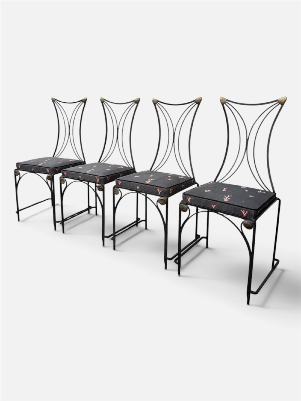 A set of six black wrought iron dining chairs featuring curved hourglass backrests, brass accents, and dark upholstered cushion seats. View V