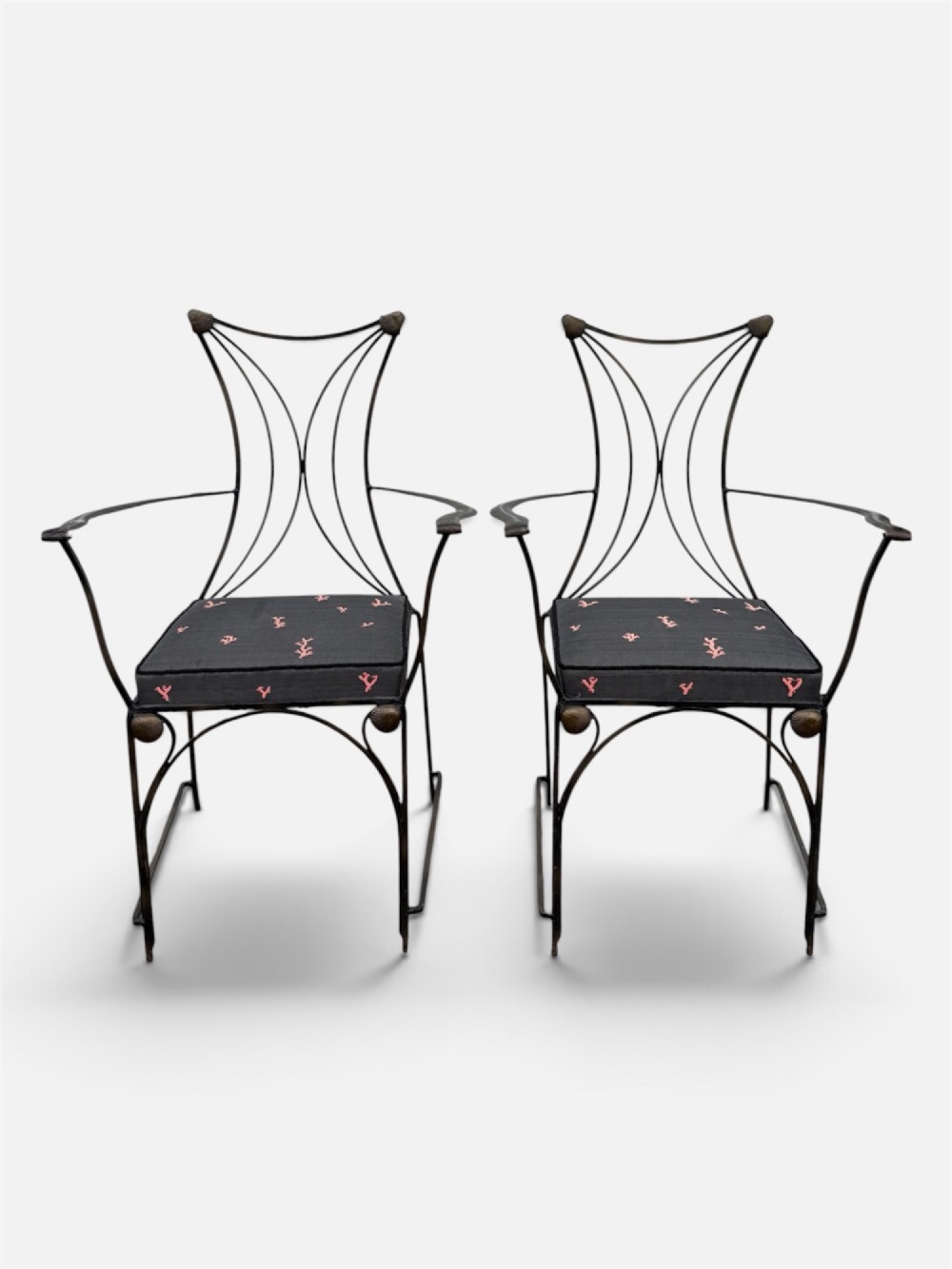A set of six black wrought iron dining chairs featuring curved hourglass backrests, brass accents, and dark upholstered cushion seats. View VI