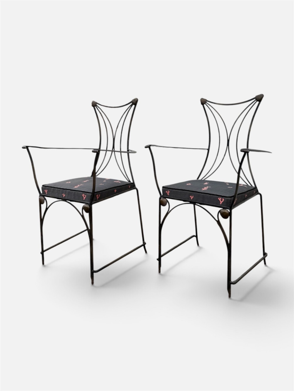 A set of six black wrought iron dining chairs featuring curved hourglass backrests, brass accents, and dark upholstered cushion seats. View VII