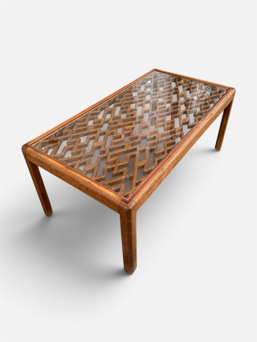 A rectangular low coffee table crafted from warm brown wood featuring an intricate geometric Chinese fretwork panel set beneath a clear glass top. View VII