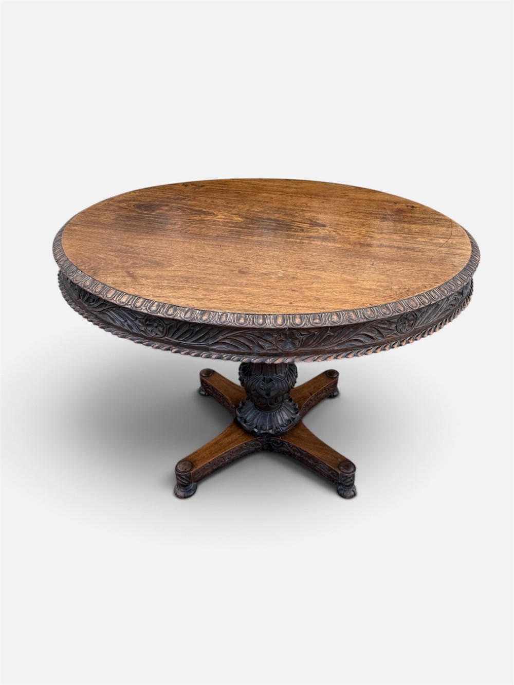 A 19th-century circular Anglo-Indian rosewood centre table featuring a carved foliate frieze, turned pedestal support, and a four-point carved platform base. View II