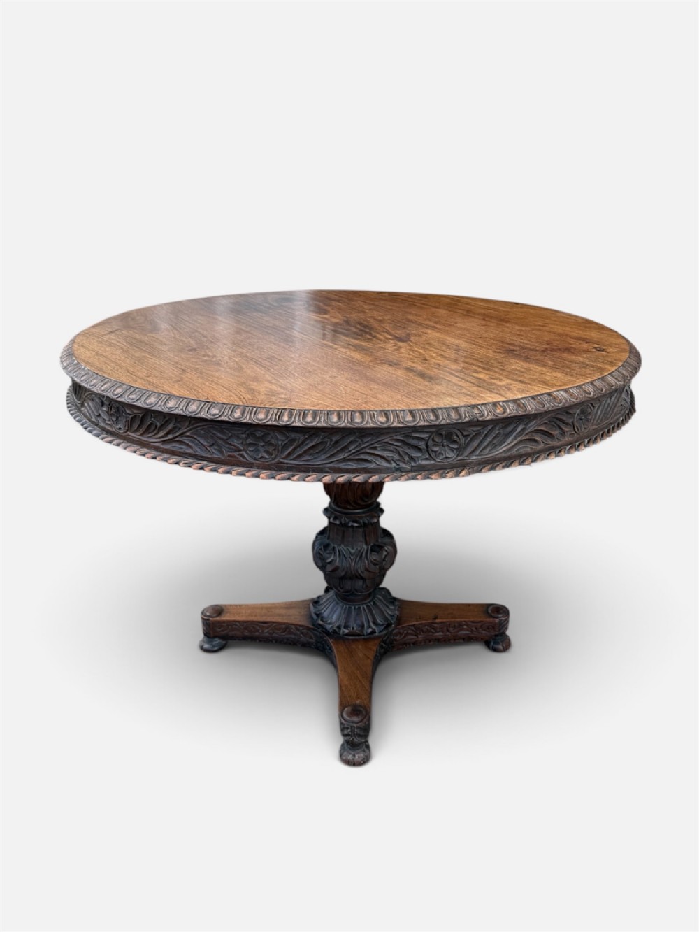 A 19th-century circular Anglo-Indian rosewood centre table featuring a carved foliate frieze, turned pedestal support, and a four-point carved platform base.