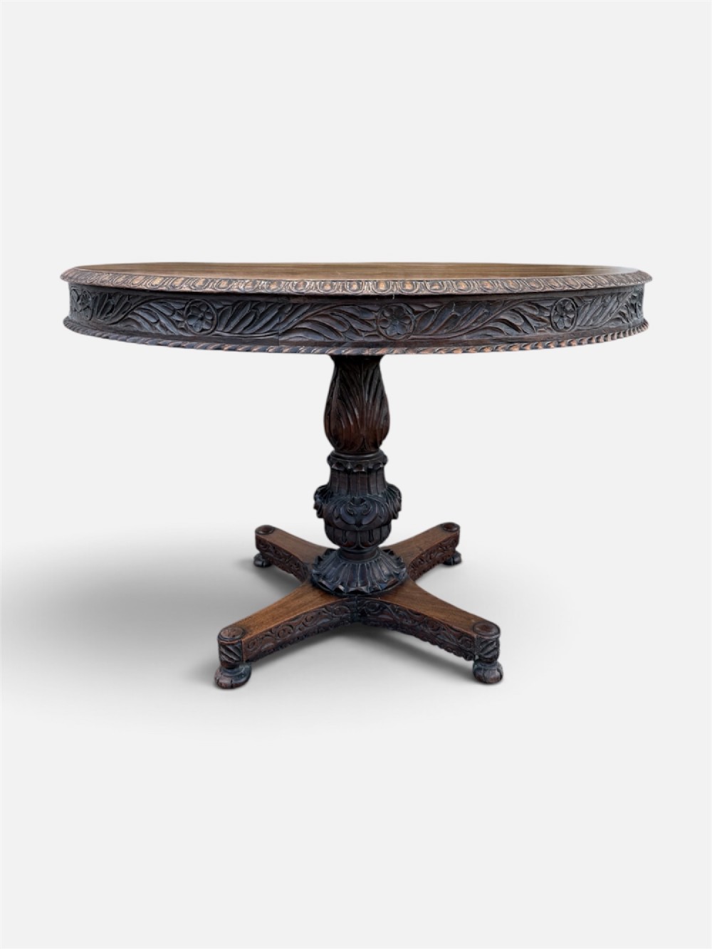 A 19th-century circular Anglo-Indian rosewood centre table featuring a carved foliate frieze, turned pedestal support, and a four-point carved platform base. View IV