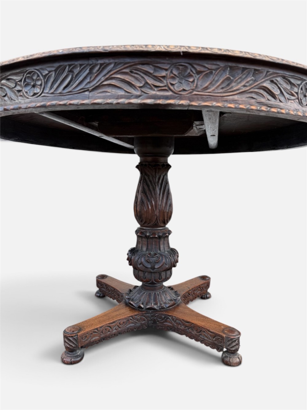 A 19th-century circular Anglo-Indian rosewood centre table featuring a carved foliate frieze, turned pedestal support, and a four-point carved platform base. View V
