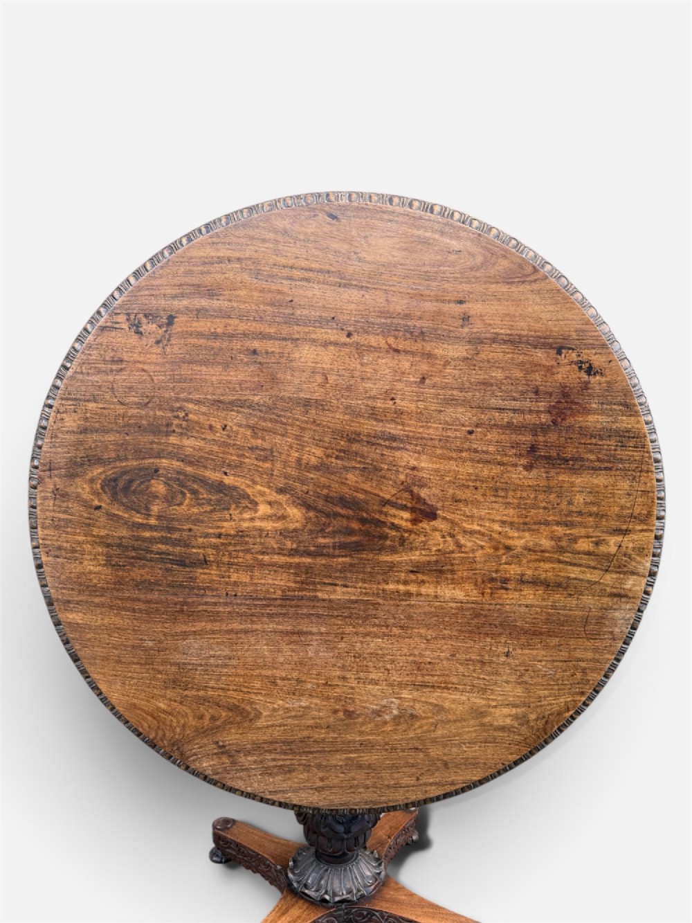 A 19th-century circular Anglo-Indian rosewood centre table featuring a carved foliate frieze, turned pedestal support, and a four-point carved platform base. View VII