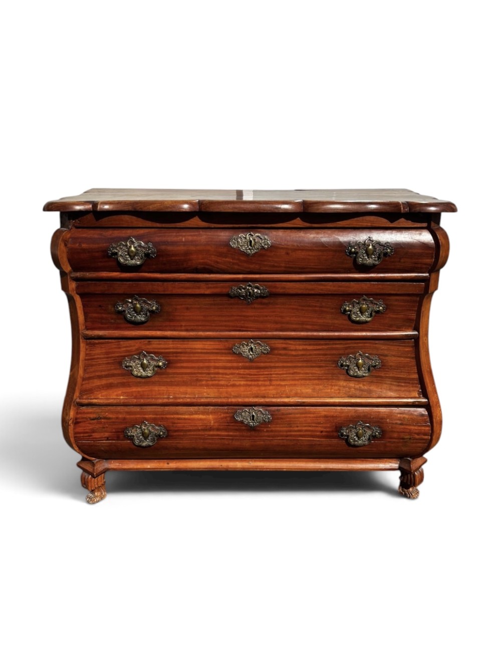 An 18th-century Dutch Colonial solid satinwood bombe chest featuring four graduated drawers, ornate brass handles, and carved feet.