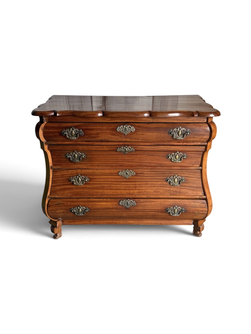 An 18th-century Dutch Colonial solid satinwood bombe chest featuring four graduated drawers, ornate brass handles, and carved feet.