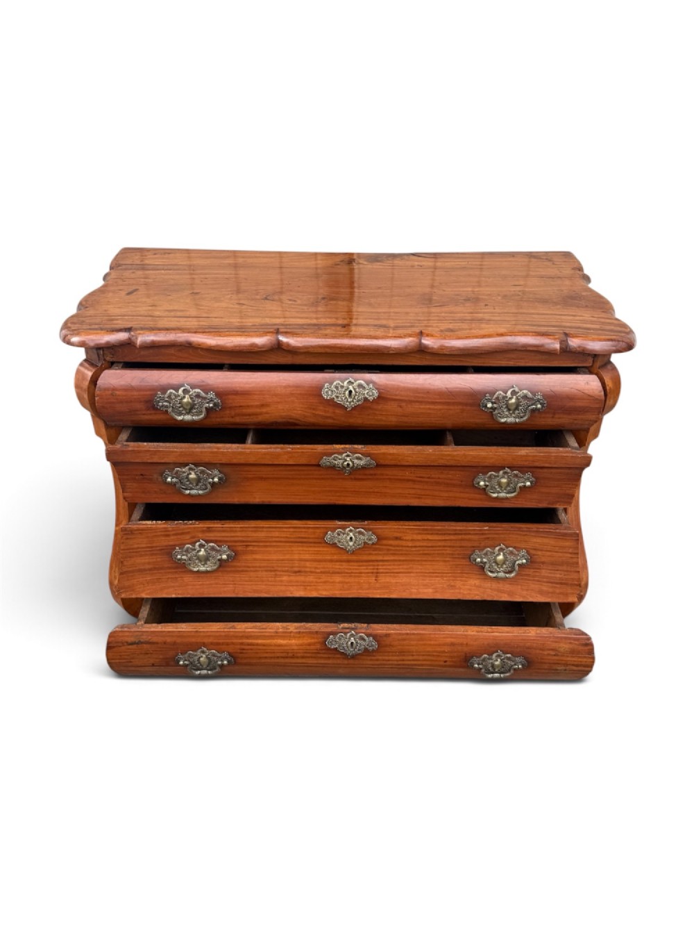 An 18th-century Dutch Colonial solid satinwood bombe chest featuring four graduated drawers, ornate brass handles, and carved feet. View V