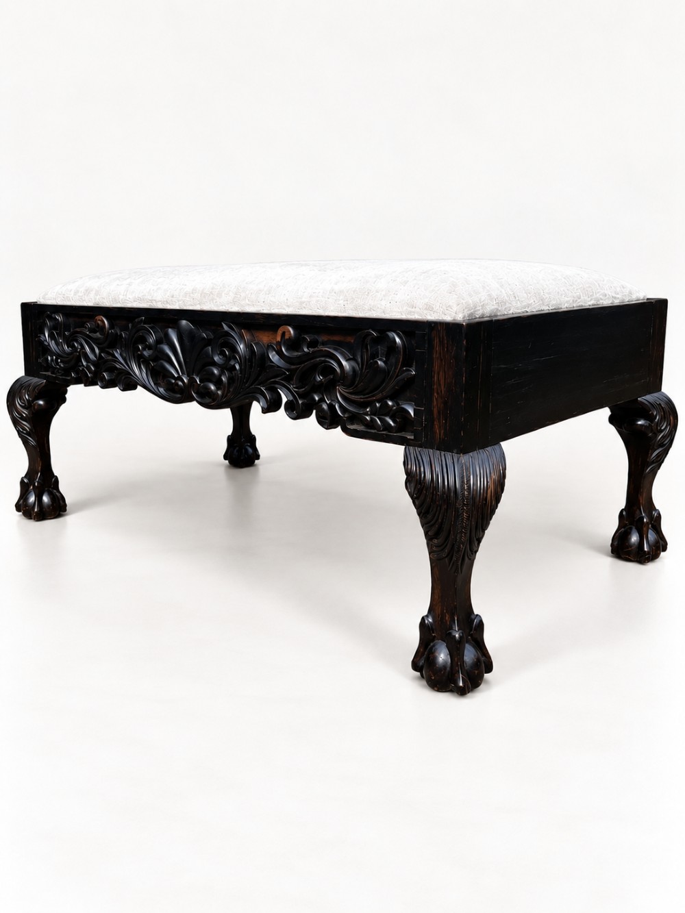 A 19th-century Ceylonese calamander wood stool featuring detailed floral relief carvings on the frame, cabriole legs with claw-and-ball feet, and neutral upholstered seat. View VI