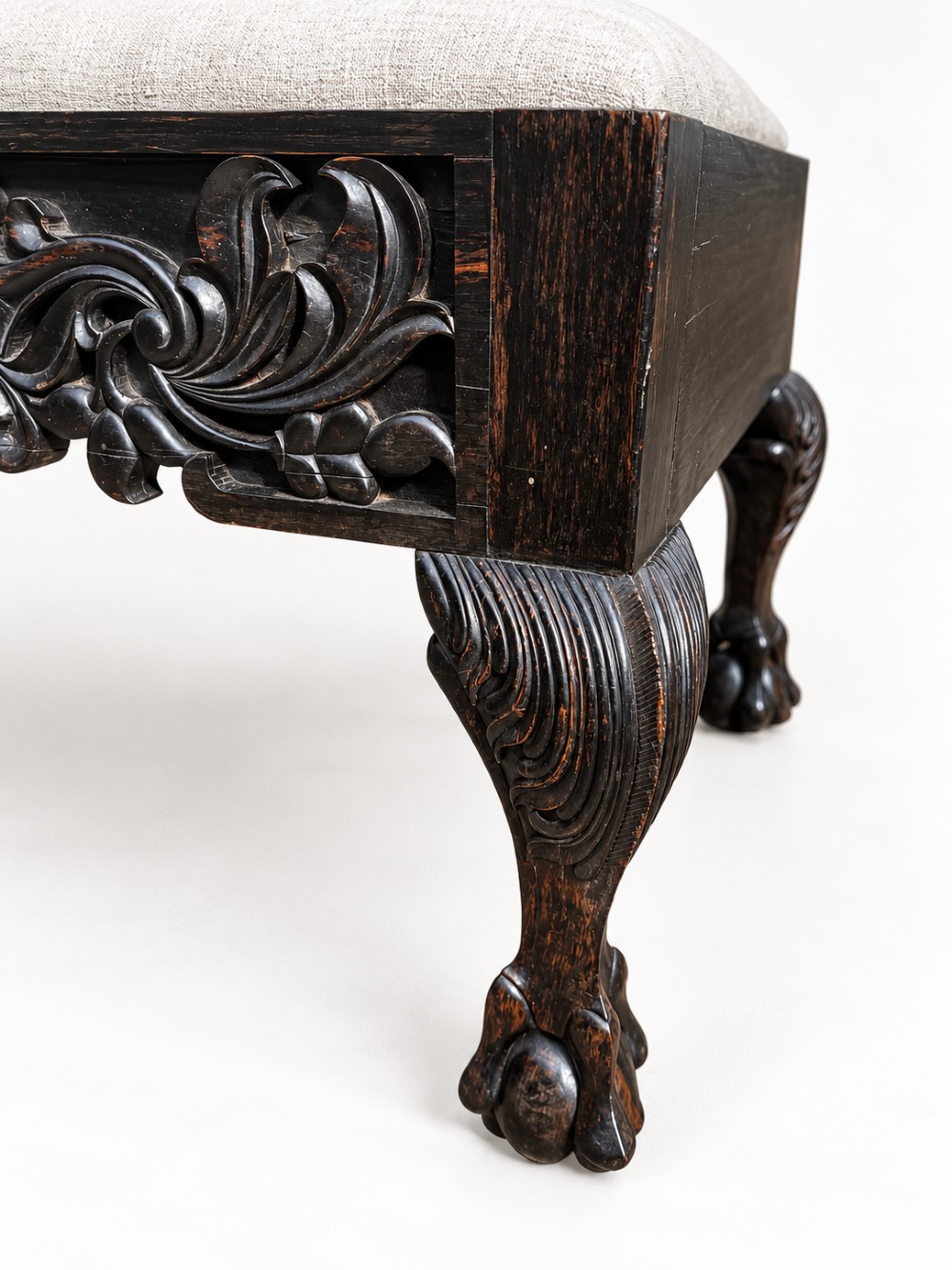 A 19th-century Ceylonese calamander wood stool featuring detailed floral relief carvings on the frame, cabriole legs with claw-and-ball feet, and neutral upholstered seat. View VII