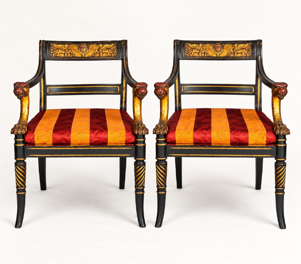A pair of black-painted and parcel-gilt Regency style armchairs featuring lion head arm terminals, spiral-turned front legs, and red and gold striped upholstery.