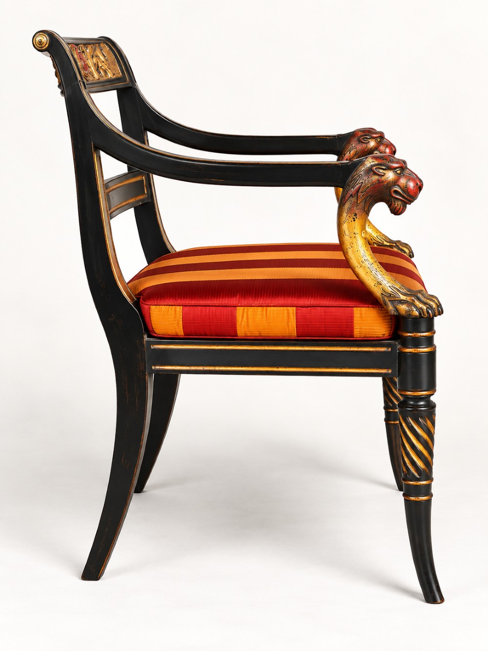 A pair of black-painted and parcel-gilt Regency style armchairs featuring lion head arm terminals, spiral-turned front legs, and red and gold striped upholstery. View V