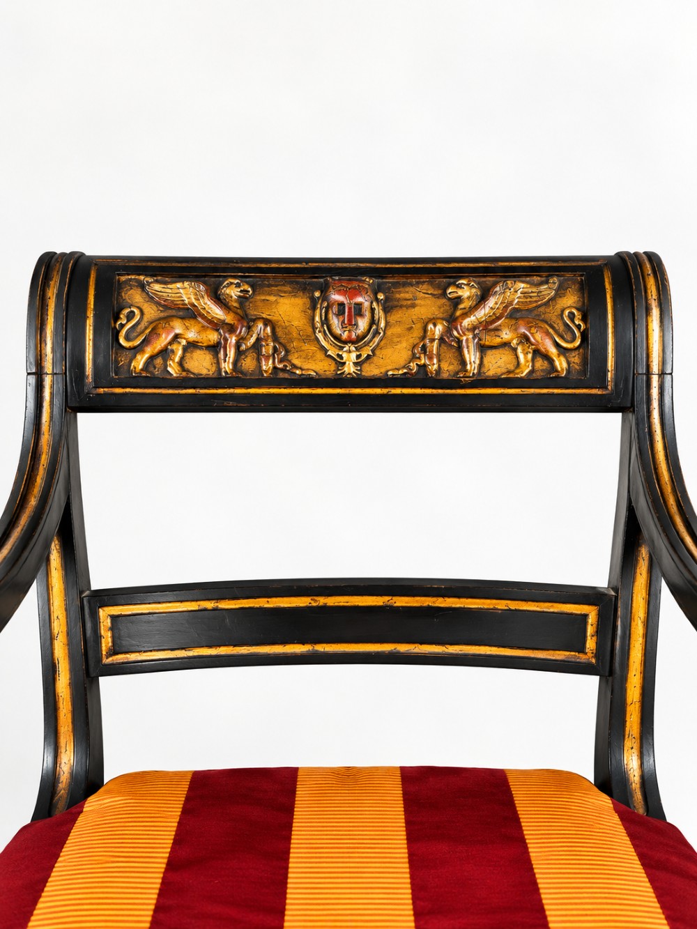 A pair of black-painted and parcel-gilt Regency style armchairs featuring lion head arm terminals, spiral-turned front legs, and red and gold striped upholstery. View VI