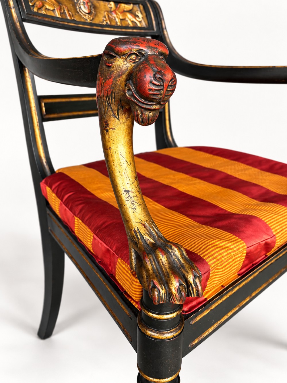 A pair of black-painted and parcel-gilt Regency style armchairs featuring lion head arm terminals, spiral-turned front legs, and red and gold striped upholstery. View VII