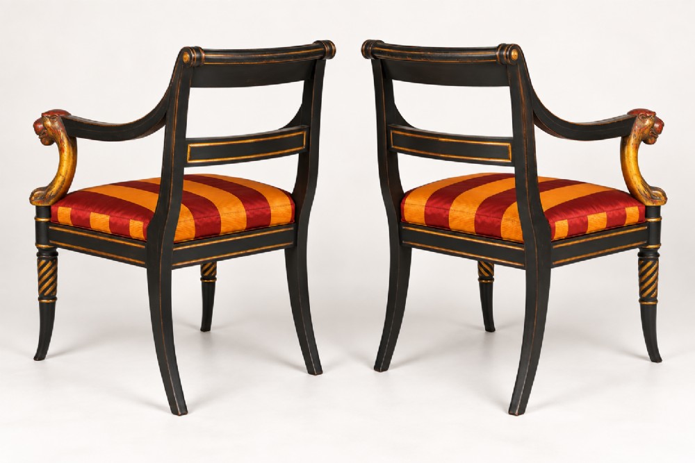 A pair of black-painted and parcel-gilt Regency style armchairs featuring lion head arm terminals, spiral-turned front legs, and red and gold striped upholstery. View VIII