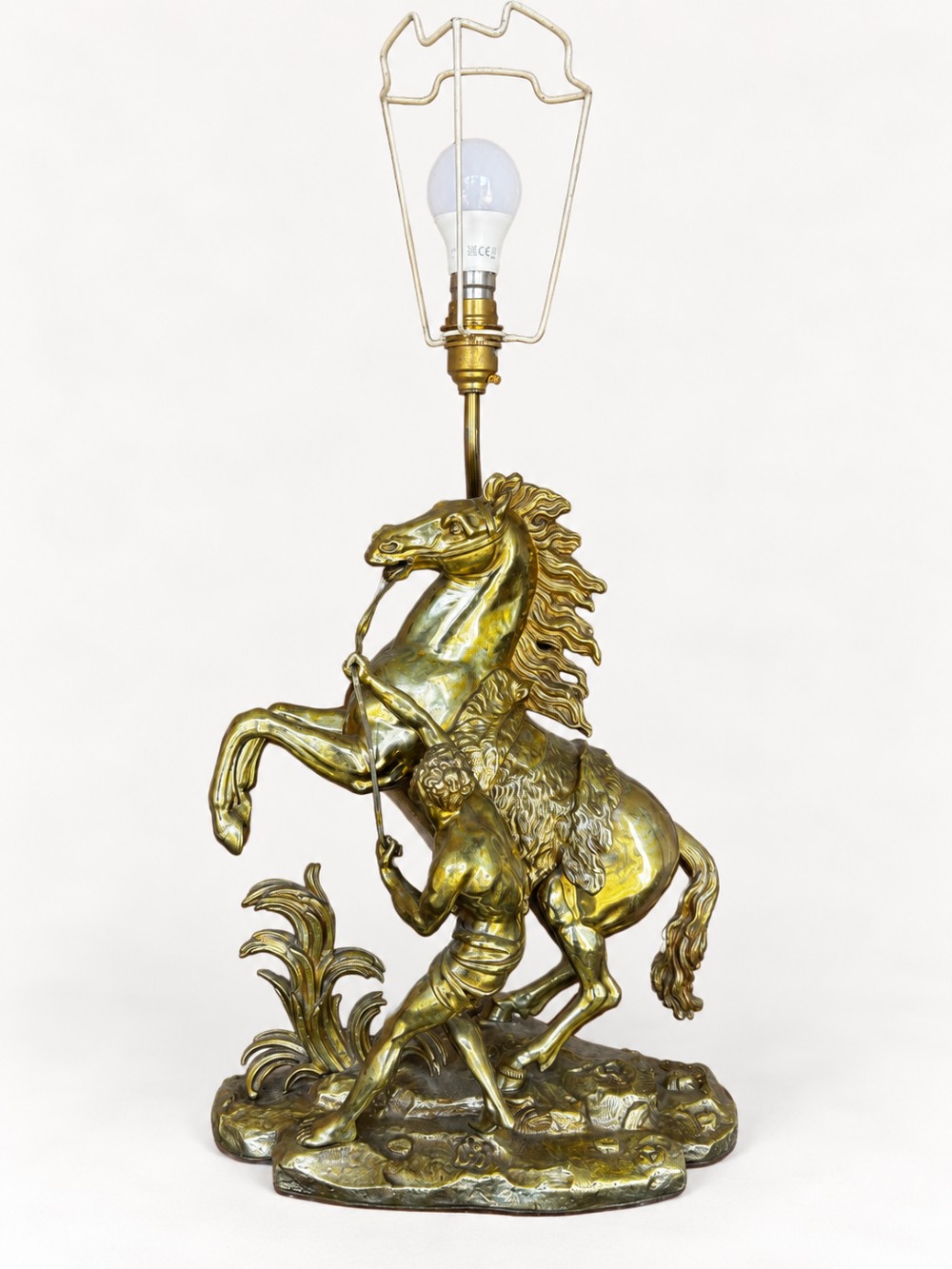 A sculptural brass table lamp depicting a rearing horse and groom after Guillaume Coustou, topped with a tall cylindrical gold leaf drum shade. View V