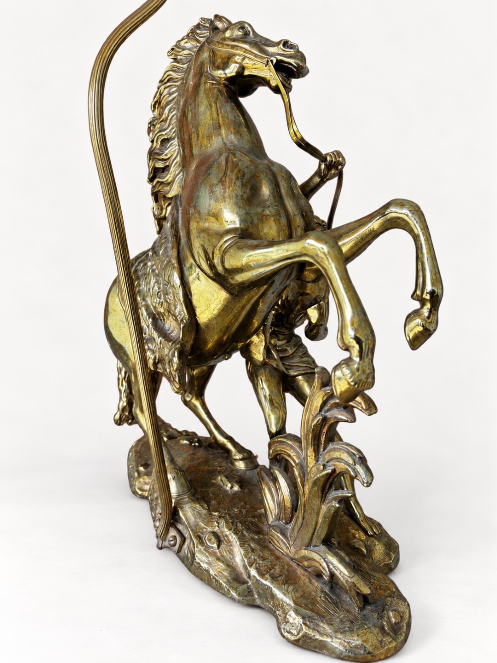 A sculptural brass table lamp depicting a rearing horse and groom after Guillaume Coustou, topped with a tall cylindrical gold leaf drum shade. View VI