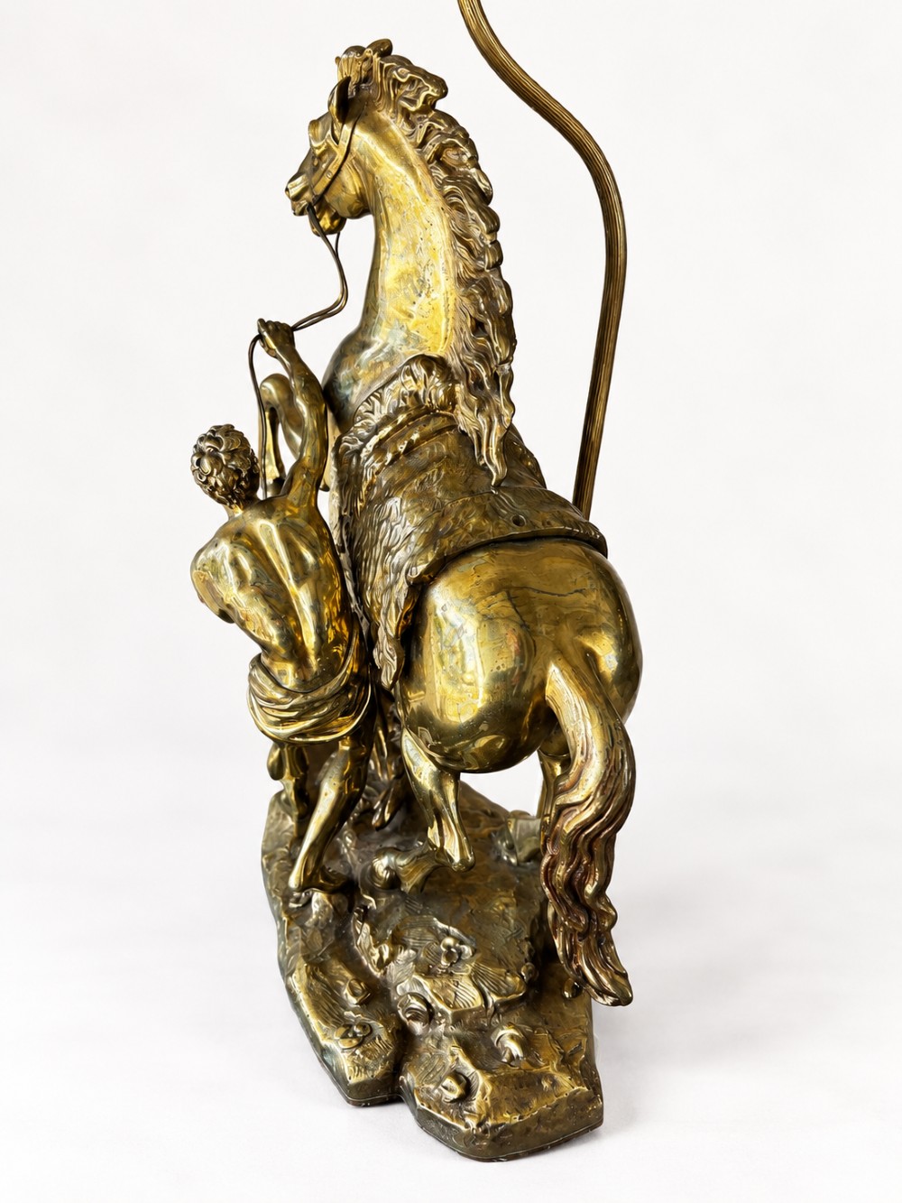 A sculptural brass table lamp depicting a rearing horse and groom after Guillaume Coustou, topped with a tall cylindrical gold leaf drum shade. View VII