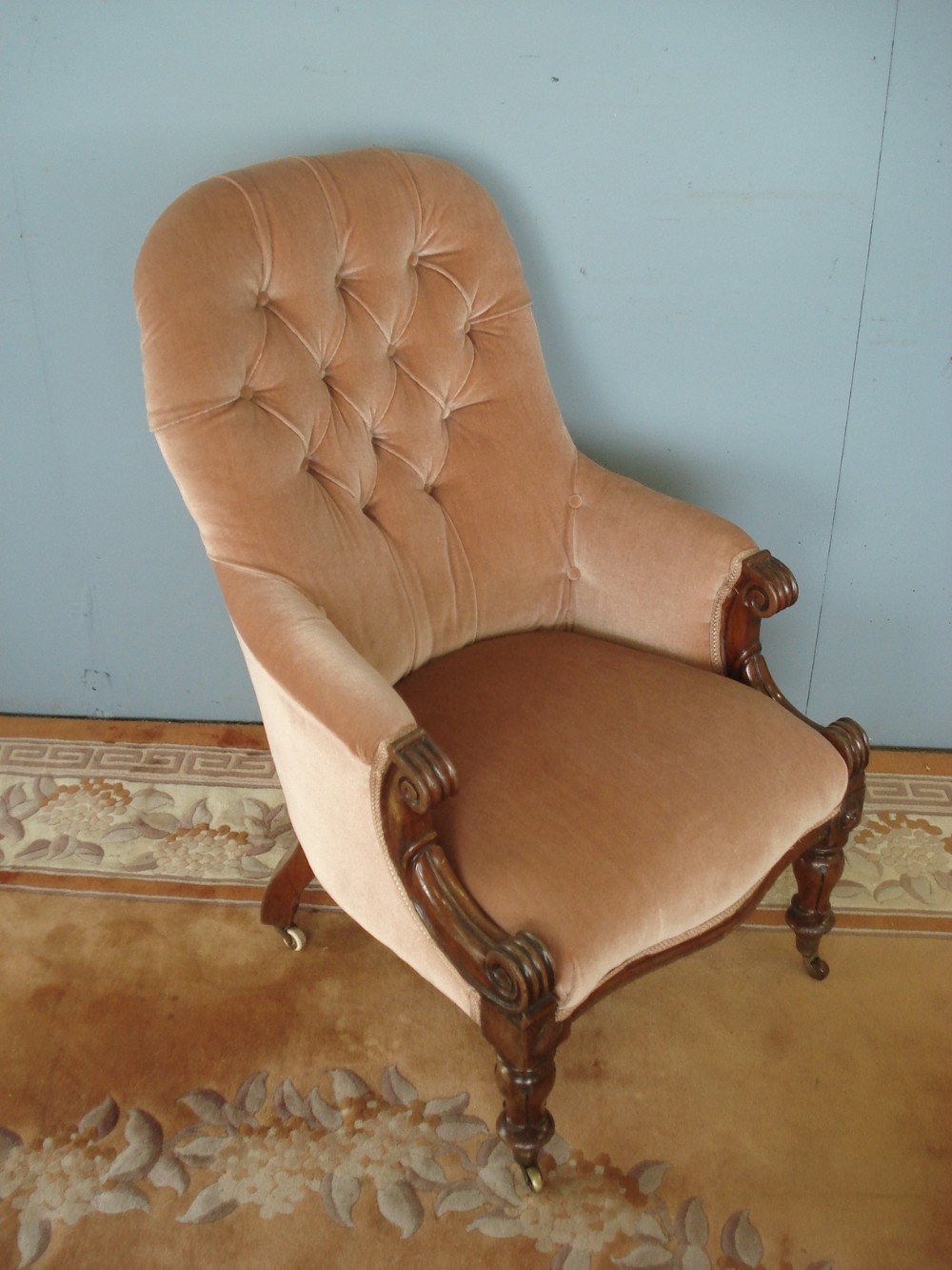 Victorian button back armchair upholstered in dusty pink velvet with carved wooden arm terminals and turned legs on brass castors.