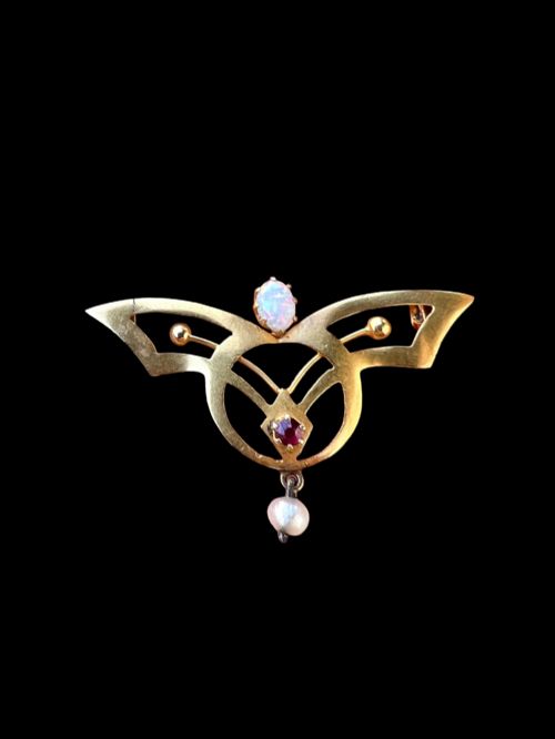fig 1. An Art Nouveau 18ct gold openwork brooch featuring a claw-set central opal, a red ruby, and a dangling pearl drop.