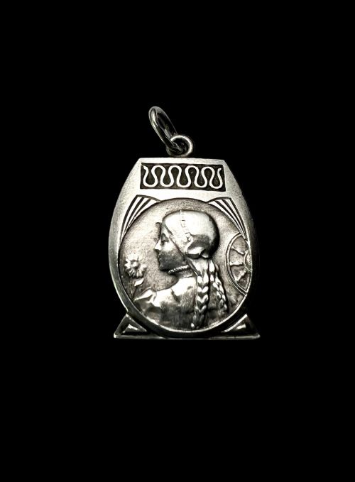 fig 1. An antique French Art Nouveau silver medallion pendant featuring a relief carving of a woman in profile holding a flower beside a spinning wheel.