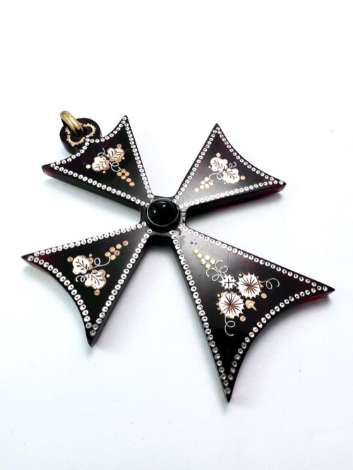 fig 1. A dark tortoiseshell cross pattee pendant decorated with gold and silver pique inlay of foliate motifs and bordered by silver pinwork with a central black cabochon.