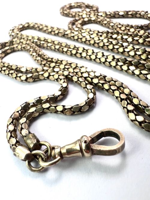 fig 1. A long yellow gold longuard chain featuring faceted textured links and an Albert swivel clip at the end on a white surface.