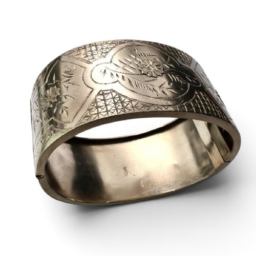 A wide Victorian sterling silver hinged cuff bangle featuring hand-engraved floral and geometric patterns across the exterior surface. View VI