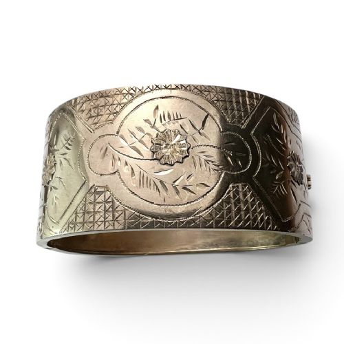 A wide Victorian sterling silver hinged cuff bangle featuring hand-engraved floral and geometric patterns across the exterior surface. View VII