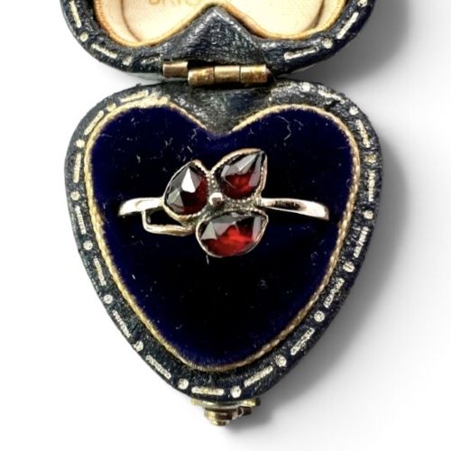 A Victorian 9ct gold ring featuring three deep red garnets arranged in a floral design set upon a slim band. View V