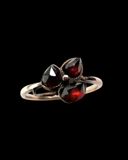 A Victorian 9ct gold ring featuring three deep red garnets arranged in a floral design set upon a slim band. View VI