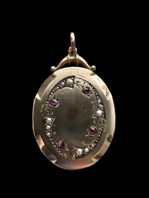 An oval 9ct yellow gold Victorian locket decorated with foliate engraving and inlaid with rubies and seed pearls. View VI