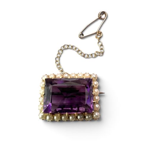 A rectangular Victorian brooch featuring a central facet-cut purple amethyst encircled by a halo of small white pearls set in 15ct gold with an attached safety chain. View III