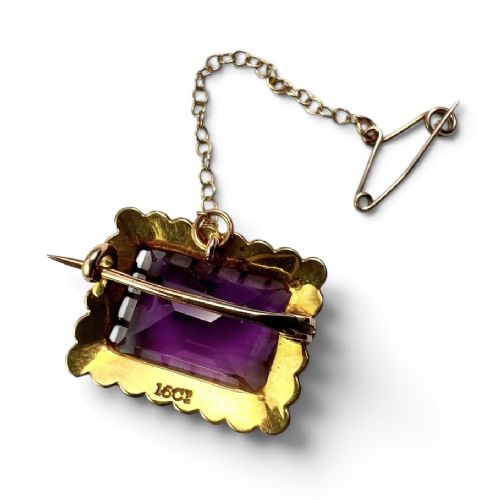 A rectangular Victorian brooch featuring a central facet-cut purple amethyst encircled by a halo of small white pearls set in 15ct gold with an attached safety chain. View IV
