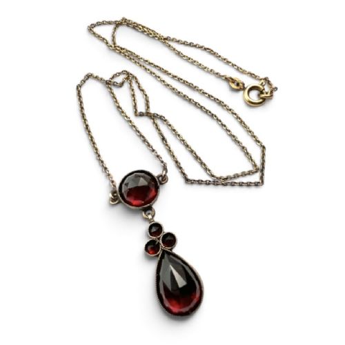 fig 1. An antique Victorian necklace featuring a fine metal chain holding a drop pendant set with multiple faceted deep red garnets.