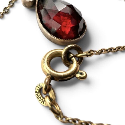 An antique Victorian necklace featuring a fine metal chain holding a drop pendant set with multiple faceted deep red garnets. View V