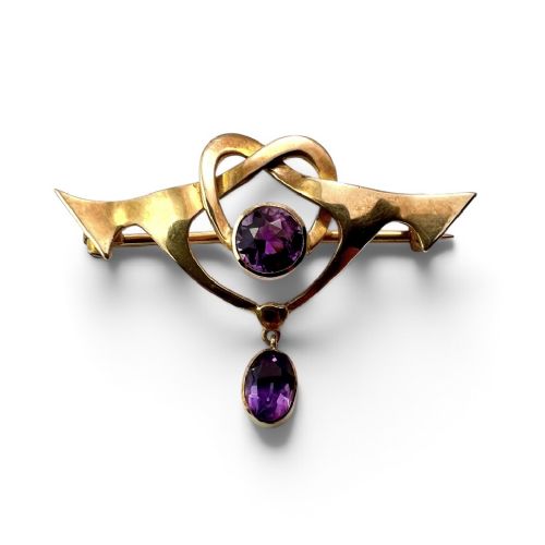 fig 1. An Art Nouveau 9ct gold brooch featuring a heart-shaped whiplash frame set with a round purple amethyst and a suspended amethyst drop, displayed inside a fitted velvet case.